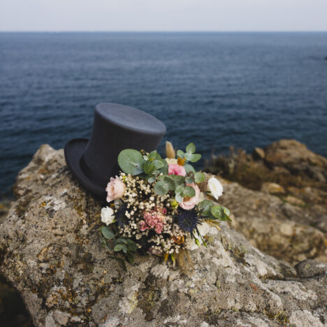 Photo de mariage en bord de mer avec un bouquet de fleurs et un chapeau haut de forme
